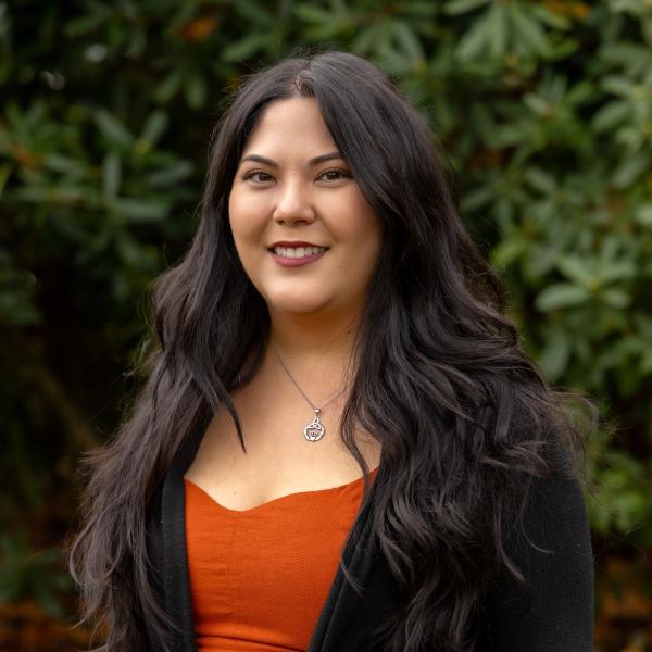 Amy Peterson wearing an orange dress, black sweater, and smiling.