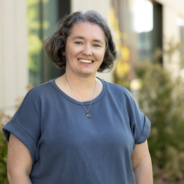 Charlotte on the OSU Cascades campus wearing a blue short sleeved shirt and smiling.